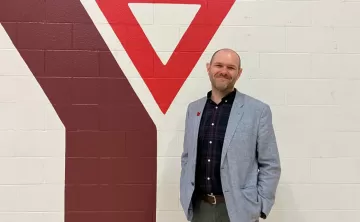 Man in sports jackets stands in front of YMCA logo