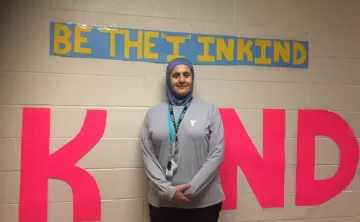YMCA child care supversior in front of a sign that says "Be the I in Kind"