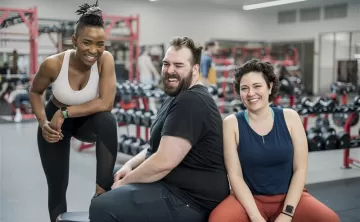 Three individuals sitting around at a gym smiling
