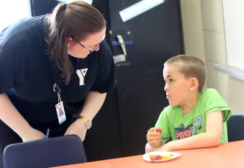 Educator bent over speaking with seated child