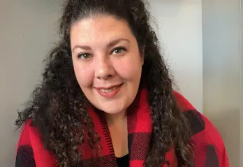 Jacqueline is wearing a red and black sweater and smiling at the camera.