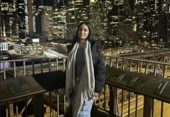 Young woman poses against the backdrop of a downtown city with skyscrapers at night.
