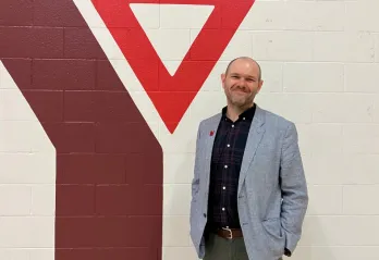Man in sports jackets stands in front of YMCA logo