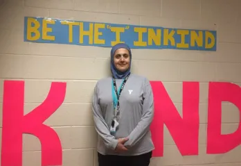 YMCA child care supversior in front of a sign that says "Be the I in Kind"