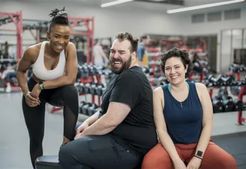 Three individuals sitting around at a gym smiling