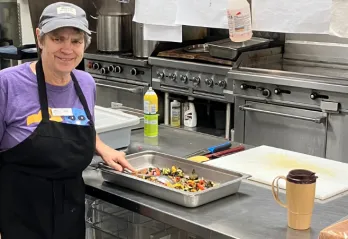 elderly woman with short grey hair in a commercial kitchen preparing vegetables