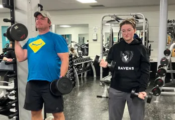 Father and daughter lift weights together in fitness centre