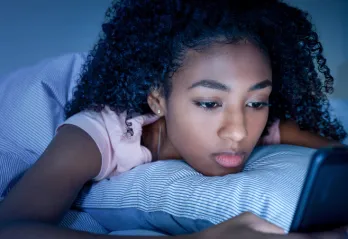young girl looking at phone in dark room, frowning