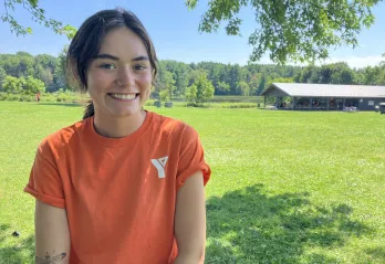 ymca day camp counsellor in orange shirt in font of green space and pavilion