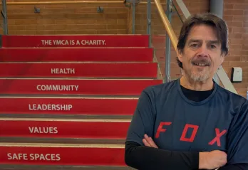 older adult male stands in front of red steps inside a building