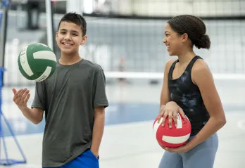 Youth holding volleyballs and smiling in a gymnasium
