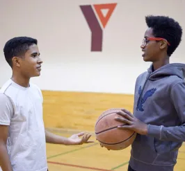 two youth talking while holding a basketball