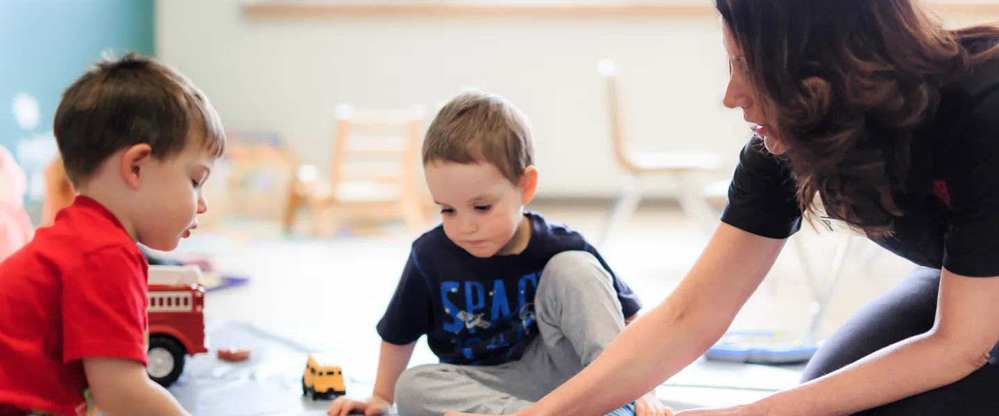 Two male preschool children and Educator playing with toy cars