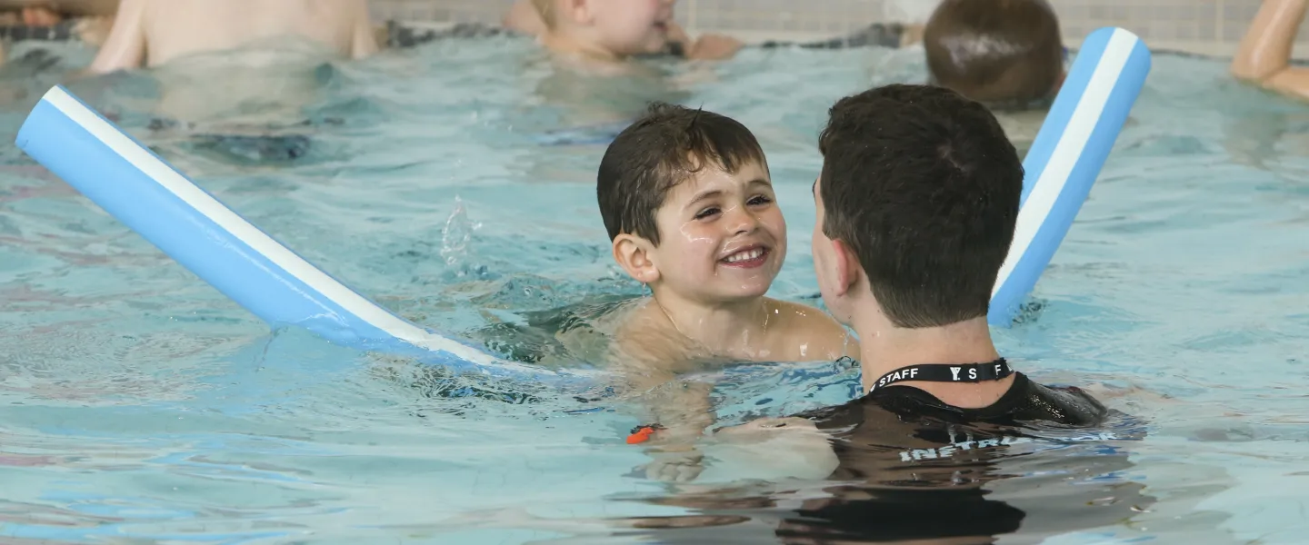 Child swimming with pool noodle and instructor
