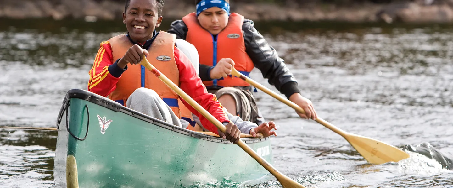 Two smiling youths paddling a canoe during Fall programming at Wanakita