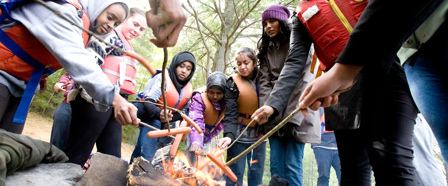 Youth roasting hotdogs on an open camp fire