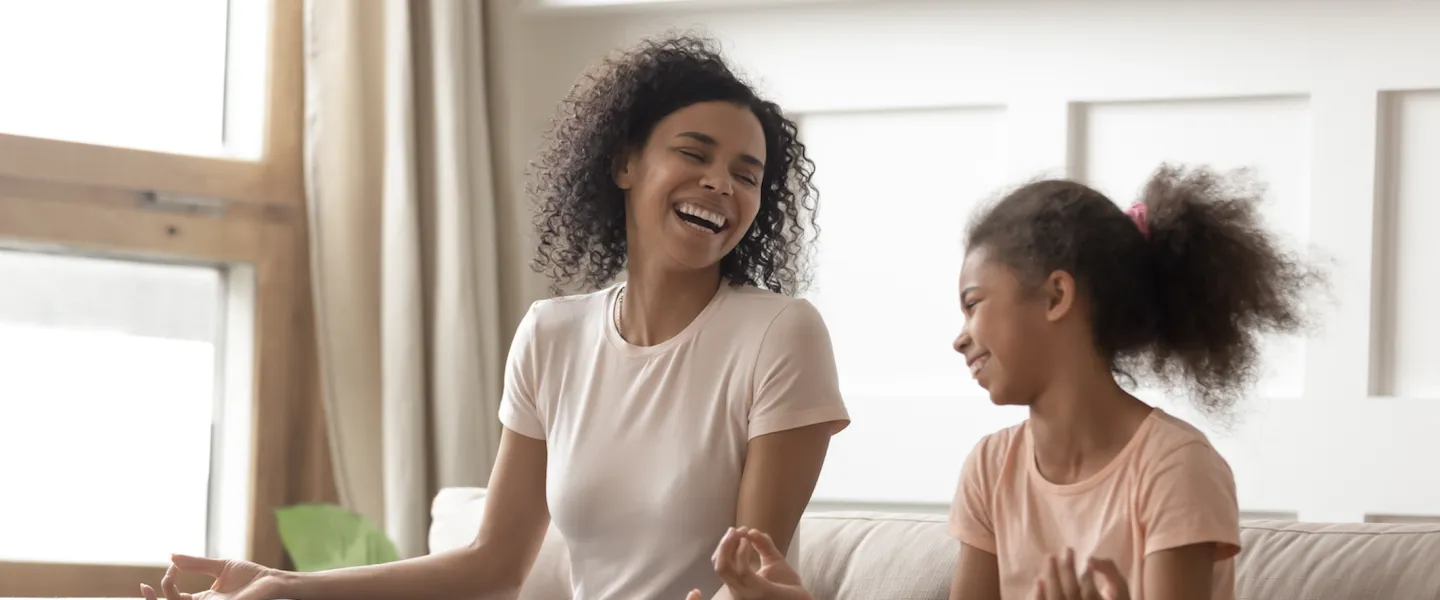 mother and daughter sit on coach laughing with one another