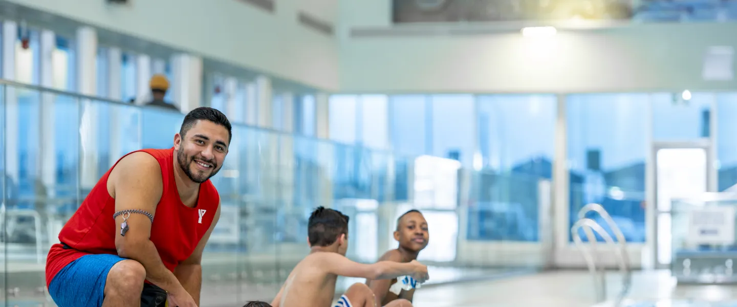 Lifeguard kneeling on deck beside children in the pool