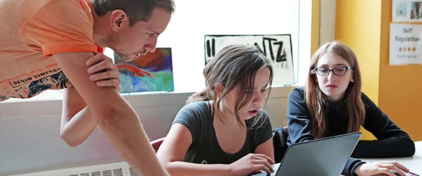 two students working on a laptop with an instructor
