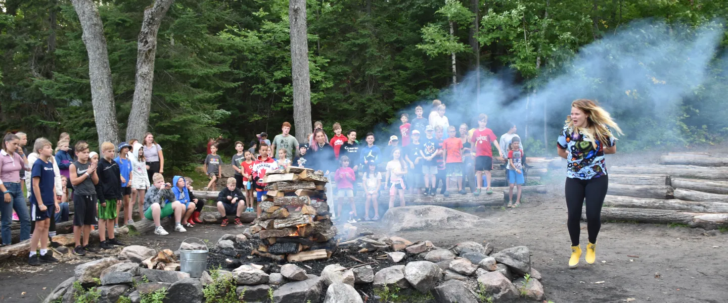 Smoke billows from a campfire as a counsellor leads the group in a song