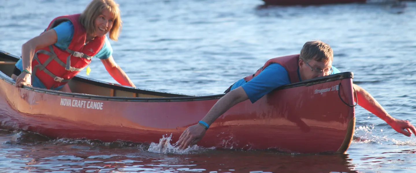 An adult male and female paddle a canoe using their hands