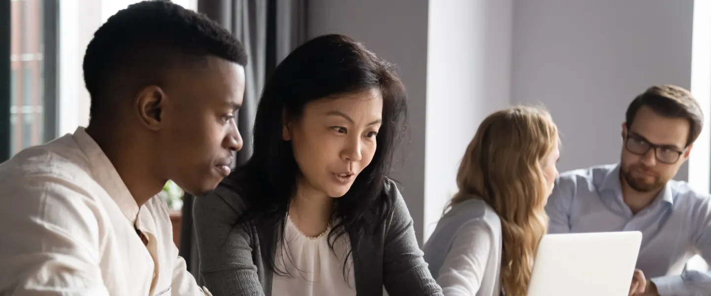 four people in two conversations, looking at laptops, talking professionally.