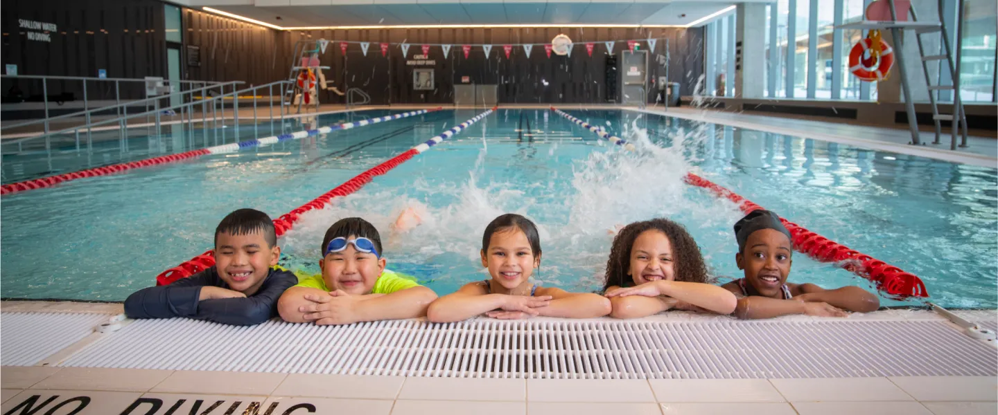 Five children in pool kicking feet and smiling