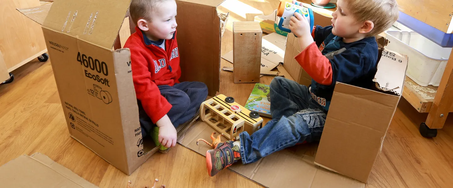 Two male preschool children building and playing with cardboard boxes