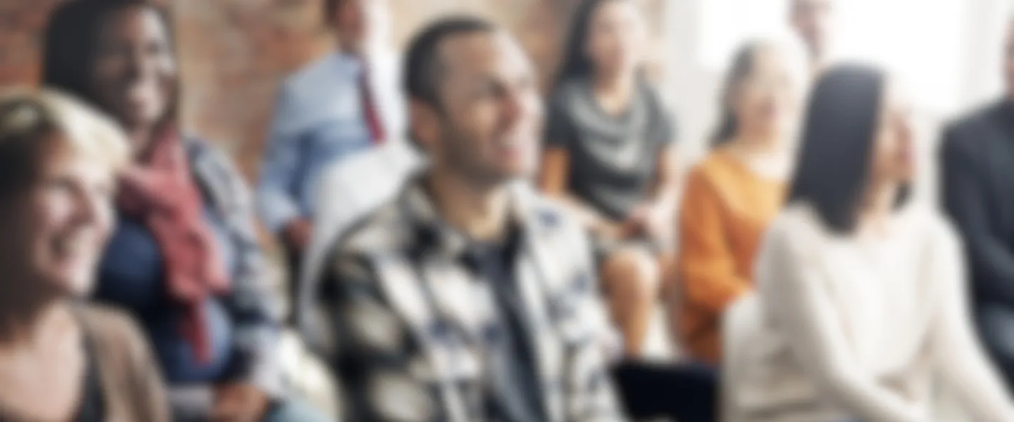 Group of diverse adults listening to a speaker and smiling, image is blurred out.