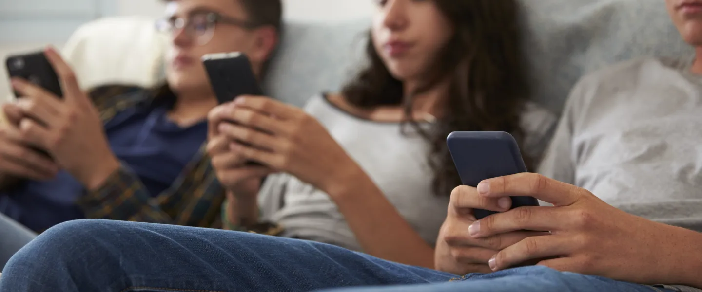 Three teenagers are sitting on the couch looking at their phones - the image is out of focus.