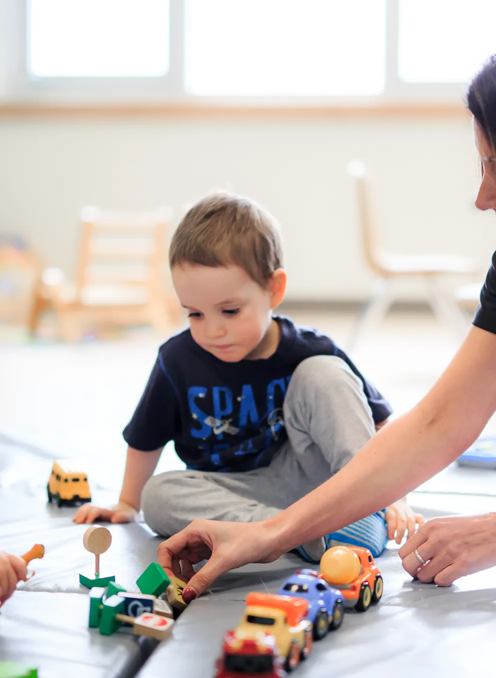 Two male preschool children and Educator playing with toy cars