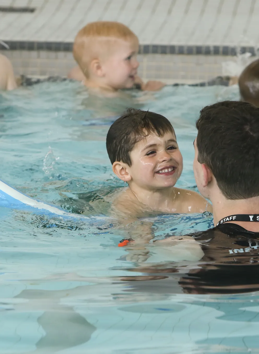 Child swimming with pool noodle and instructor