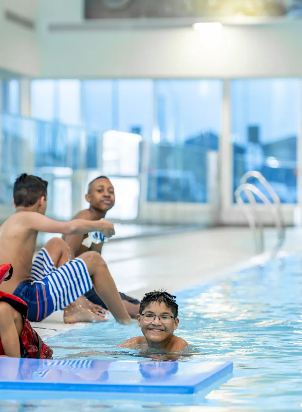Lifeguard kneeling on deck beside children in the pool