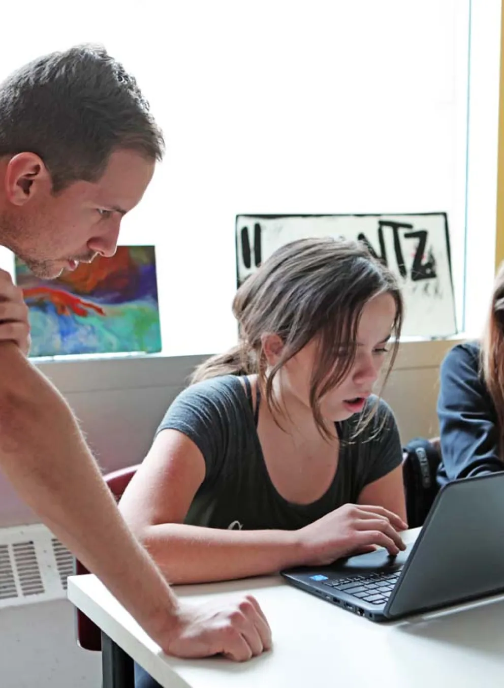 two students working on a laptop with an instructor