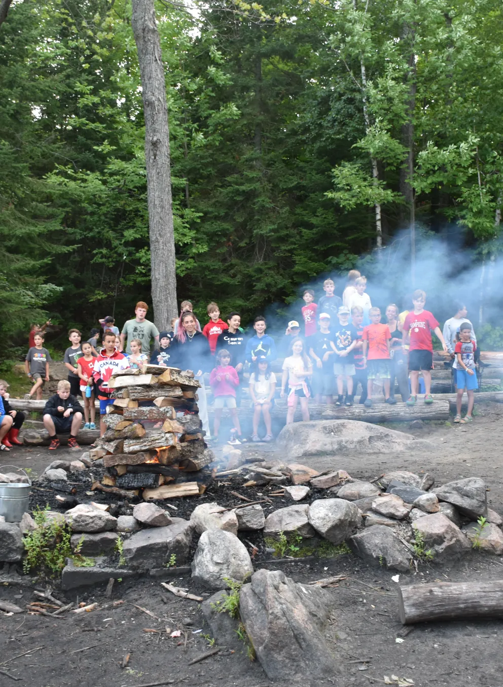 Smoke billows from a campfire as a counsellor leads the group in a song