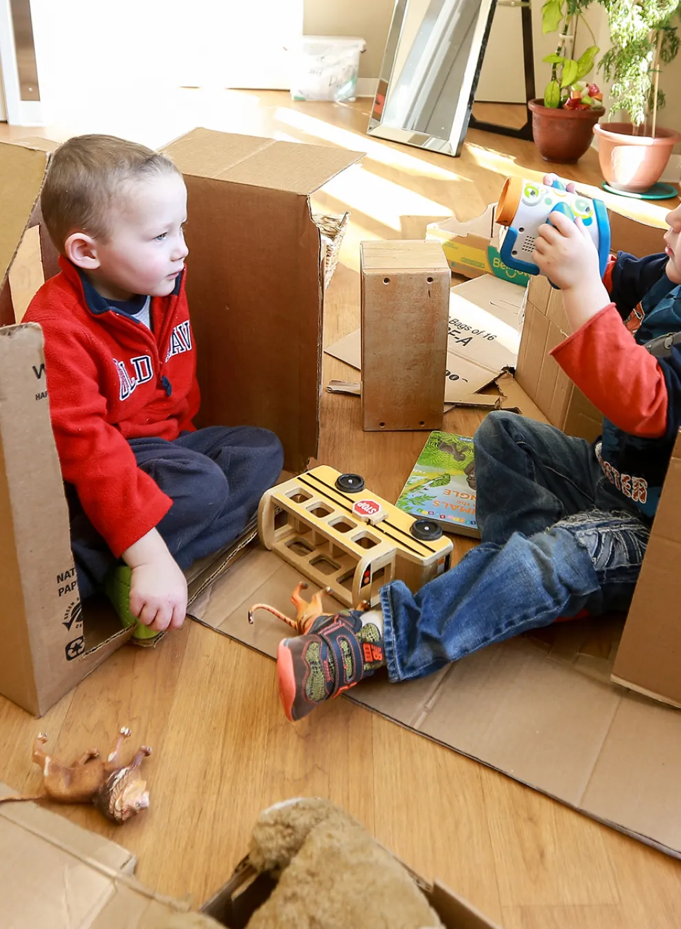 Two male preschool children building and playing with cardboard boxes