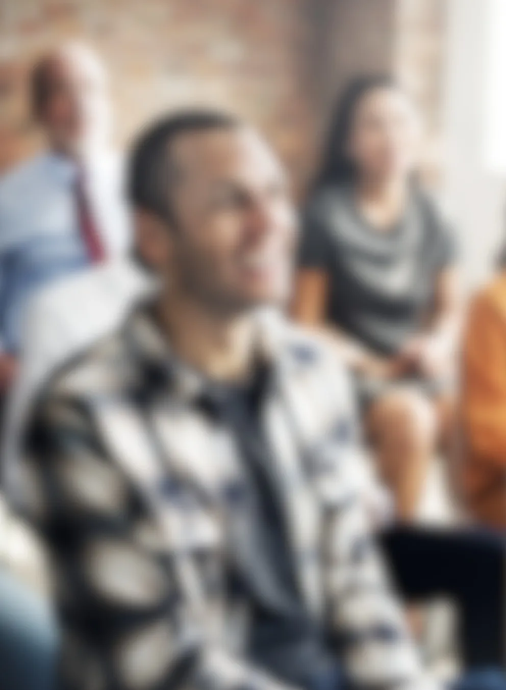 Group of diverse adults listening to a speaker and smiling, image is blurred out.