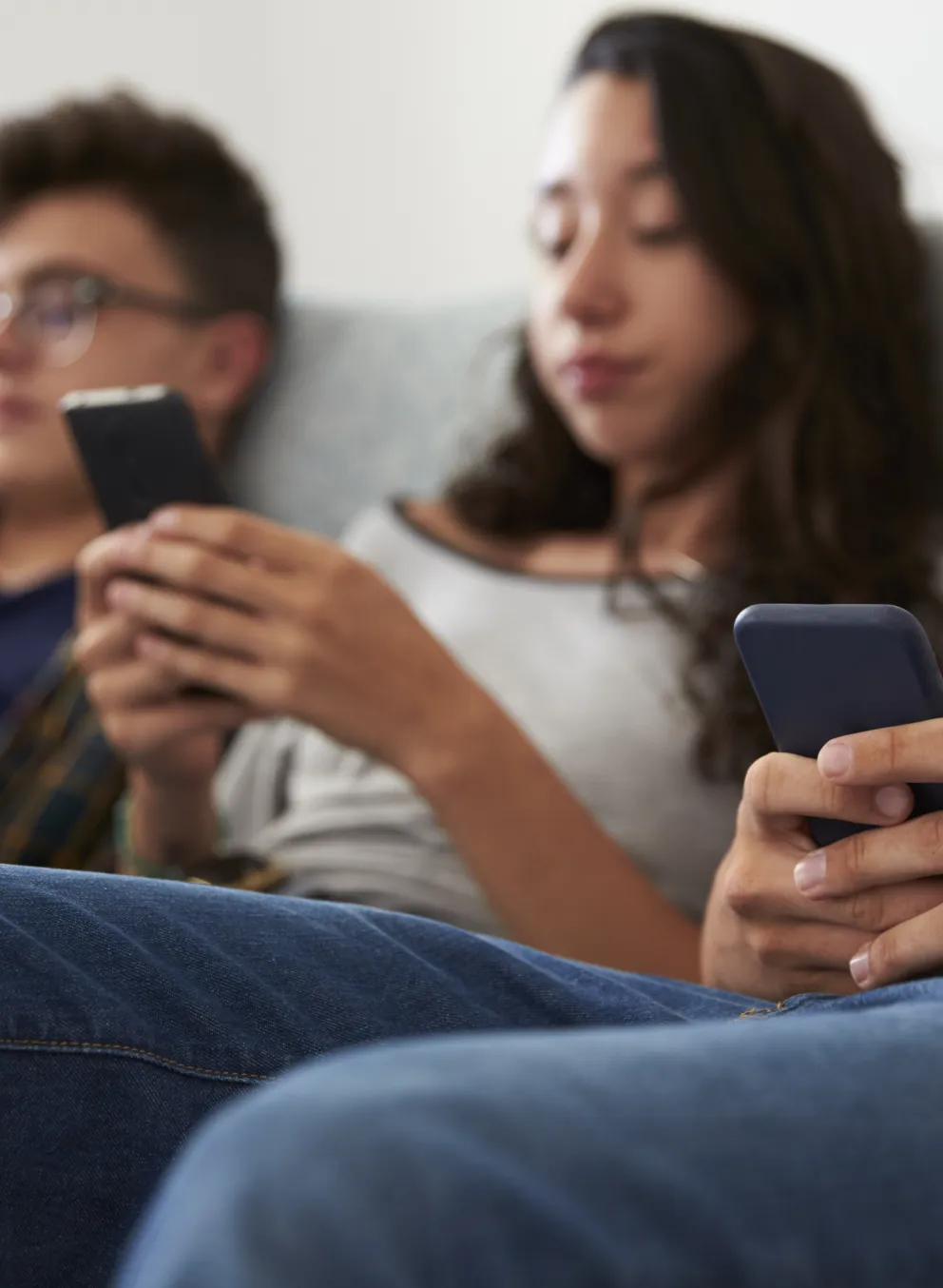 Three teenagers are sitting on the couch looking at their phones - the image is out of focus.