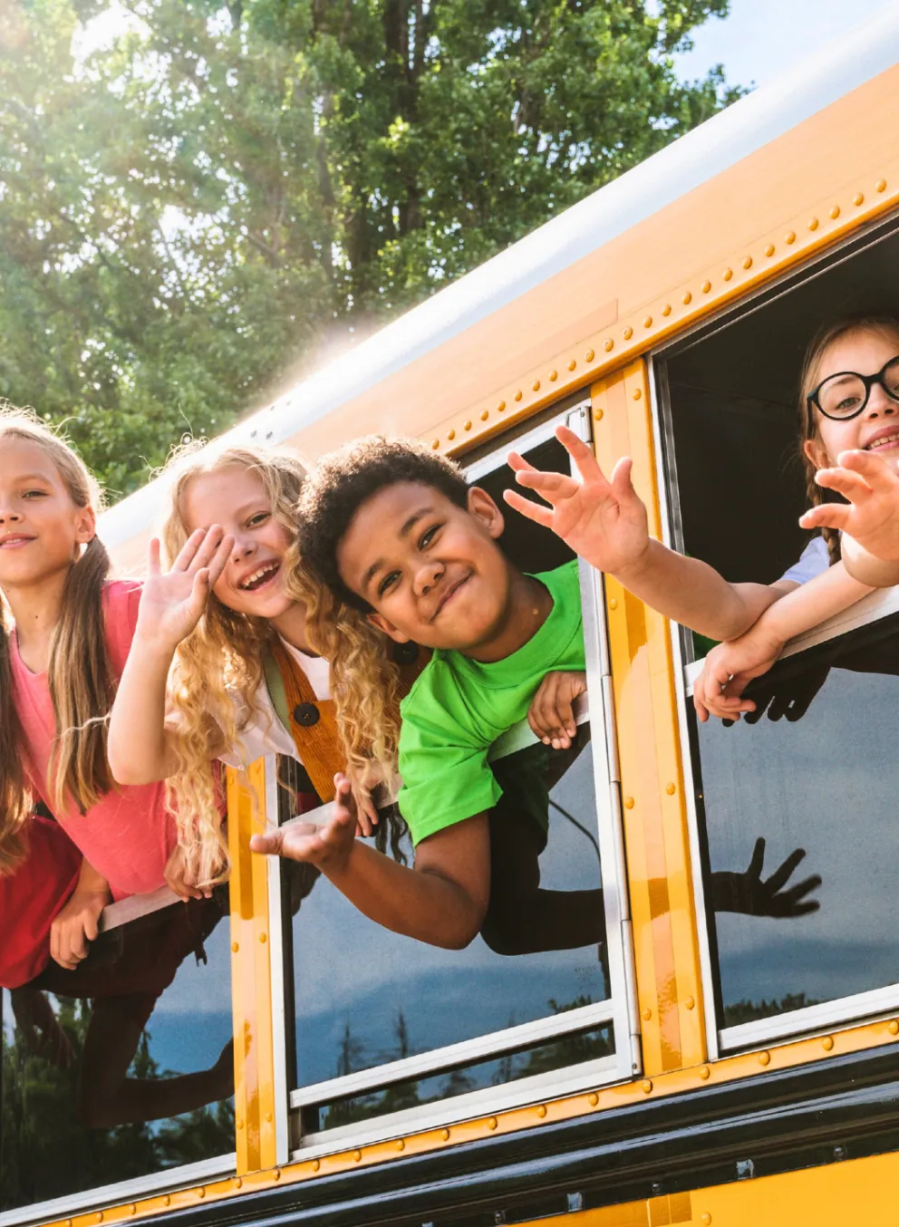 Group of kids smiling and waving from school bus