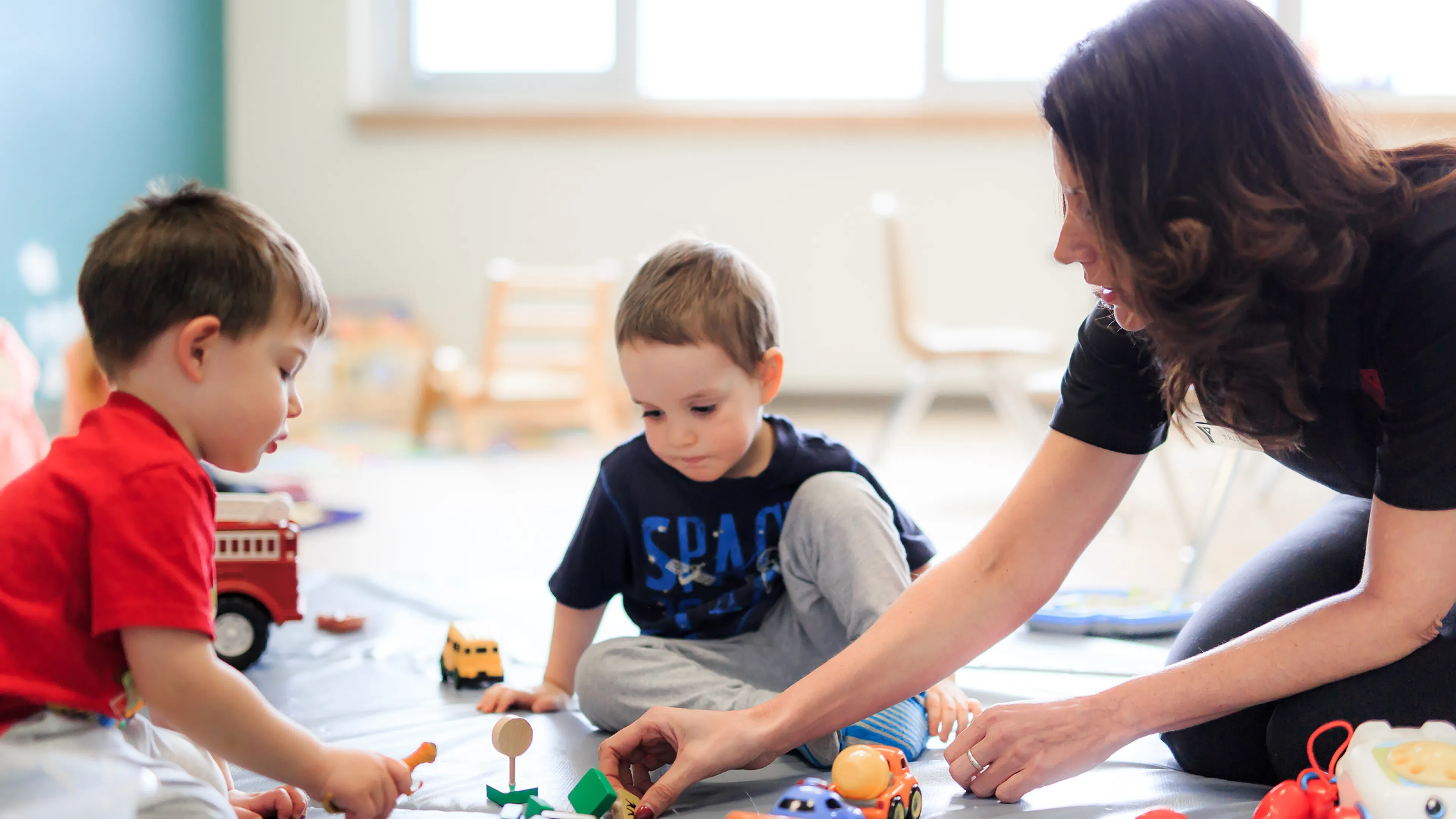 Two male preschool children and Educator playing with toy cars