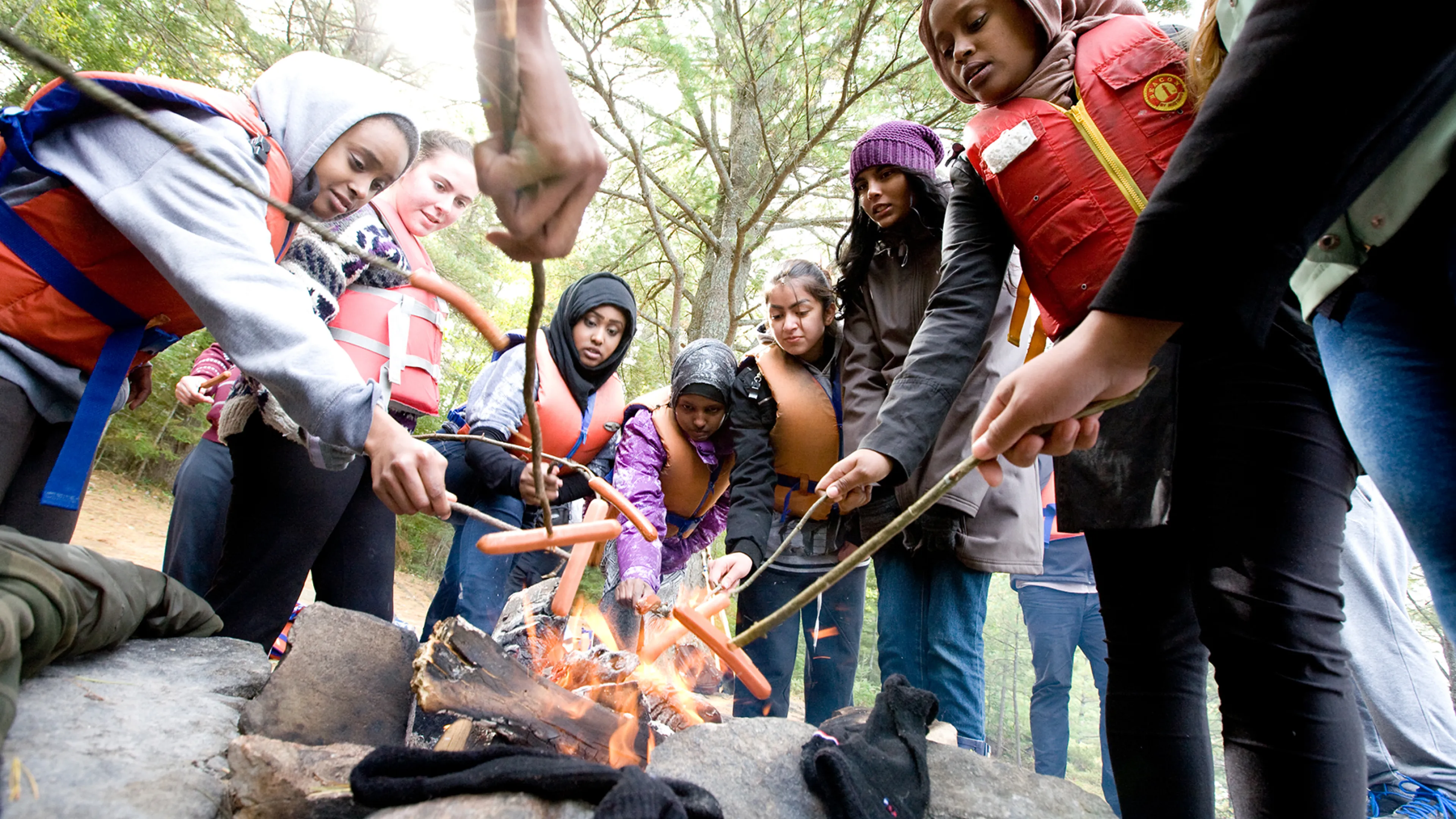 Youth roasting hotdogs on an open camp fire