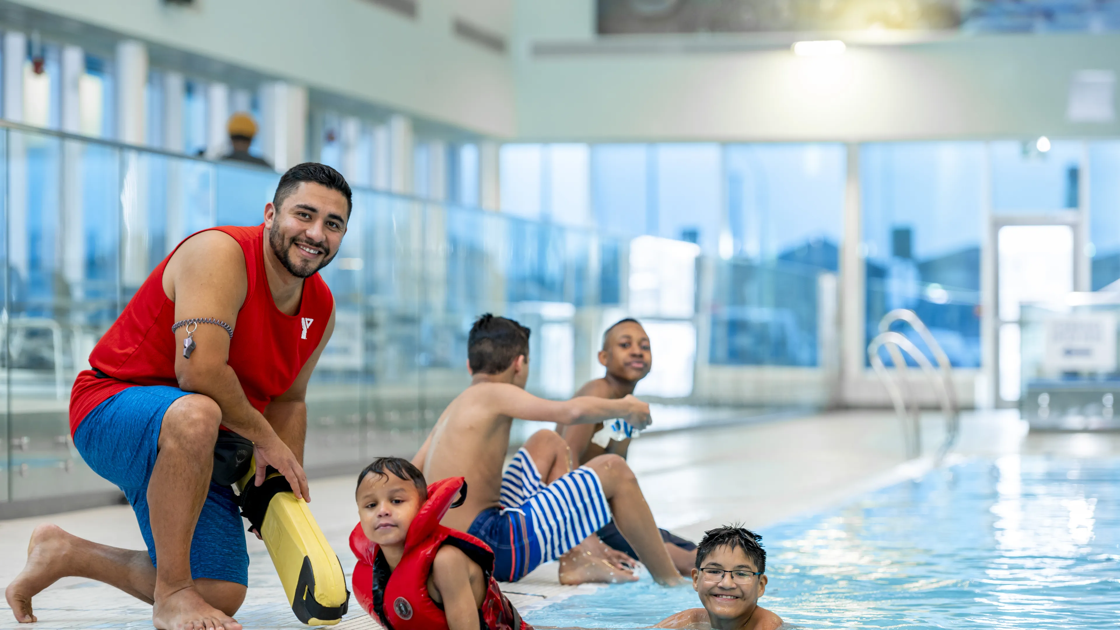 Lifeguard kneeling on deck beside children in the pool