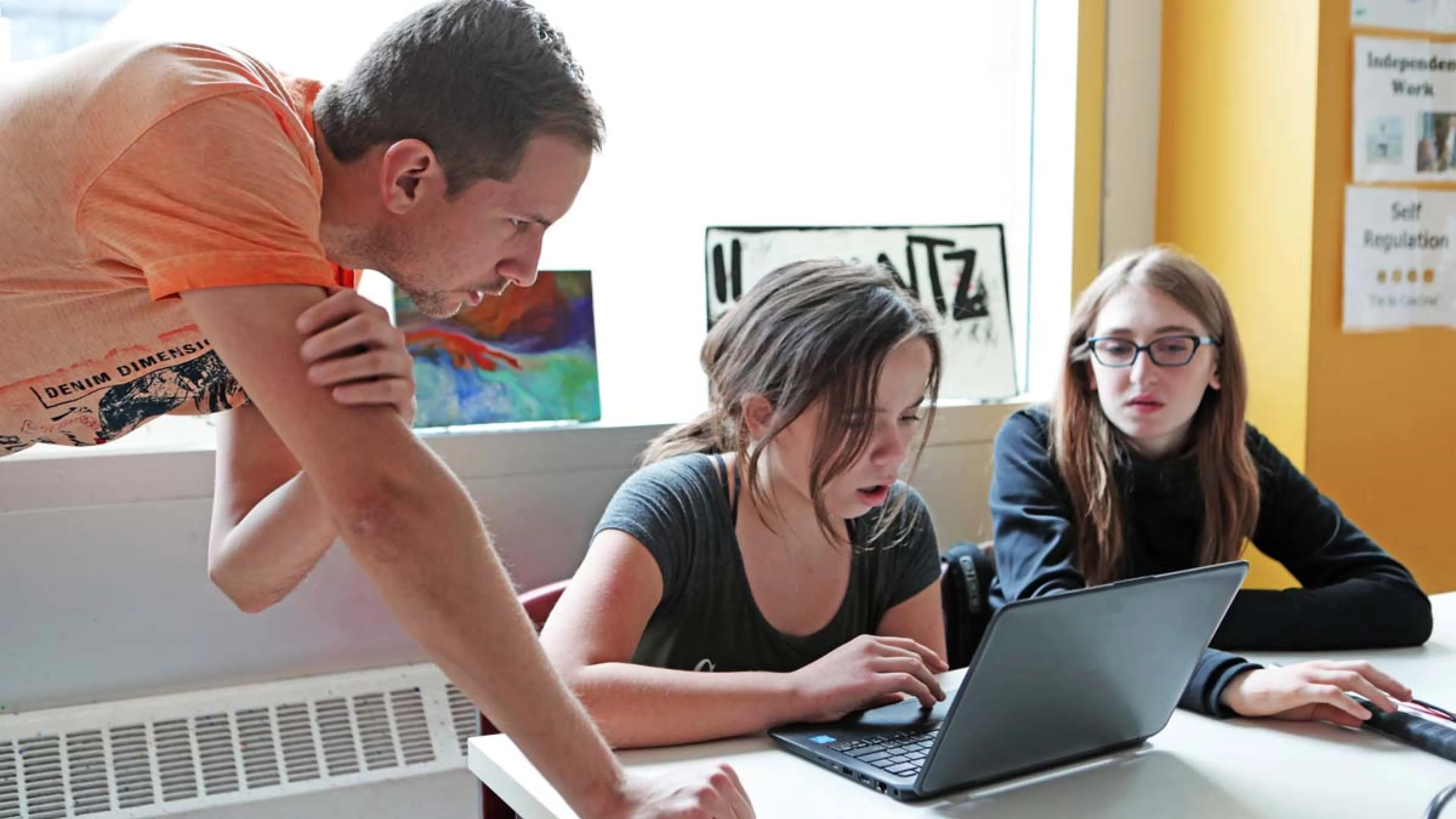 two students working on a laptop with an instructor
