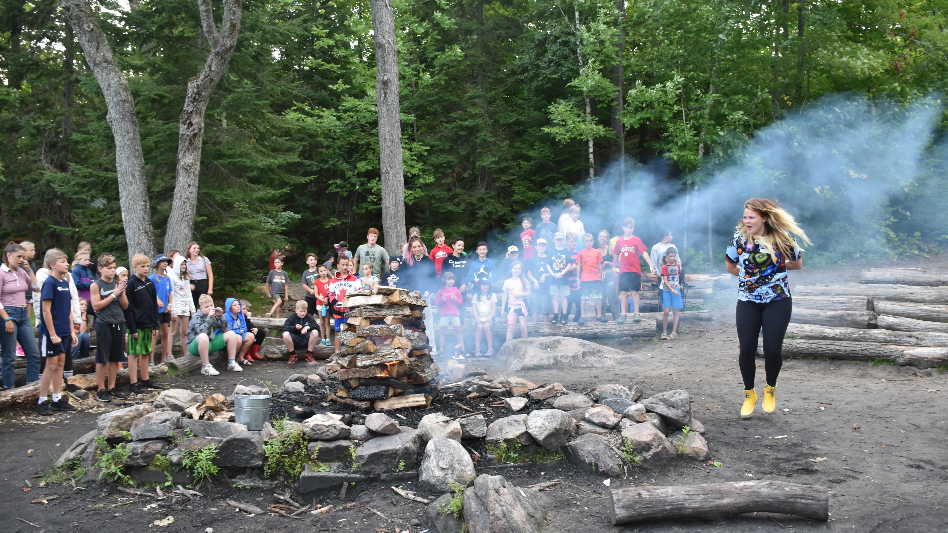 Smoke billows from a campfire as a counsellor leads the group in a song
