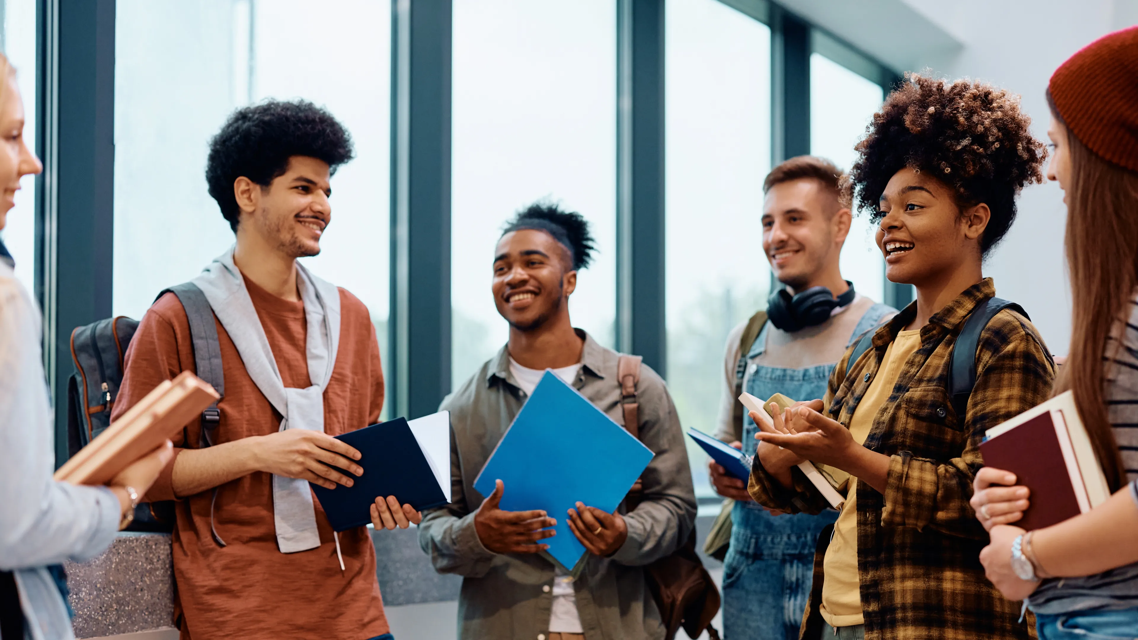 6 young people standing in a  circle talking, smiling.
