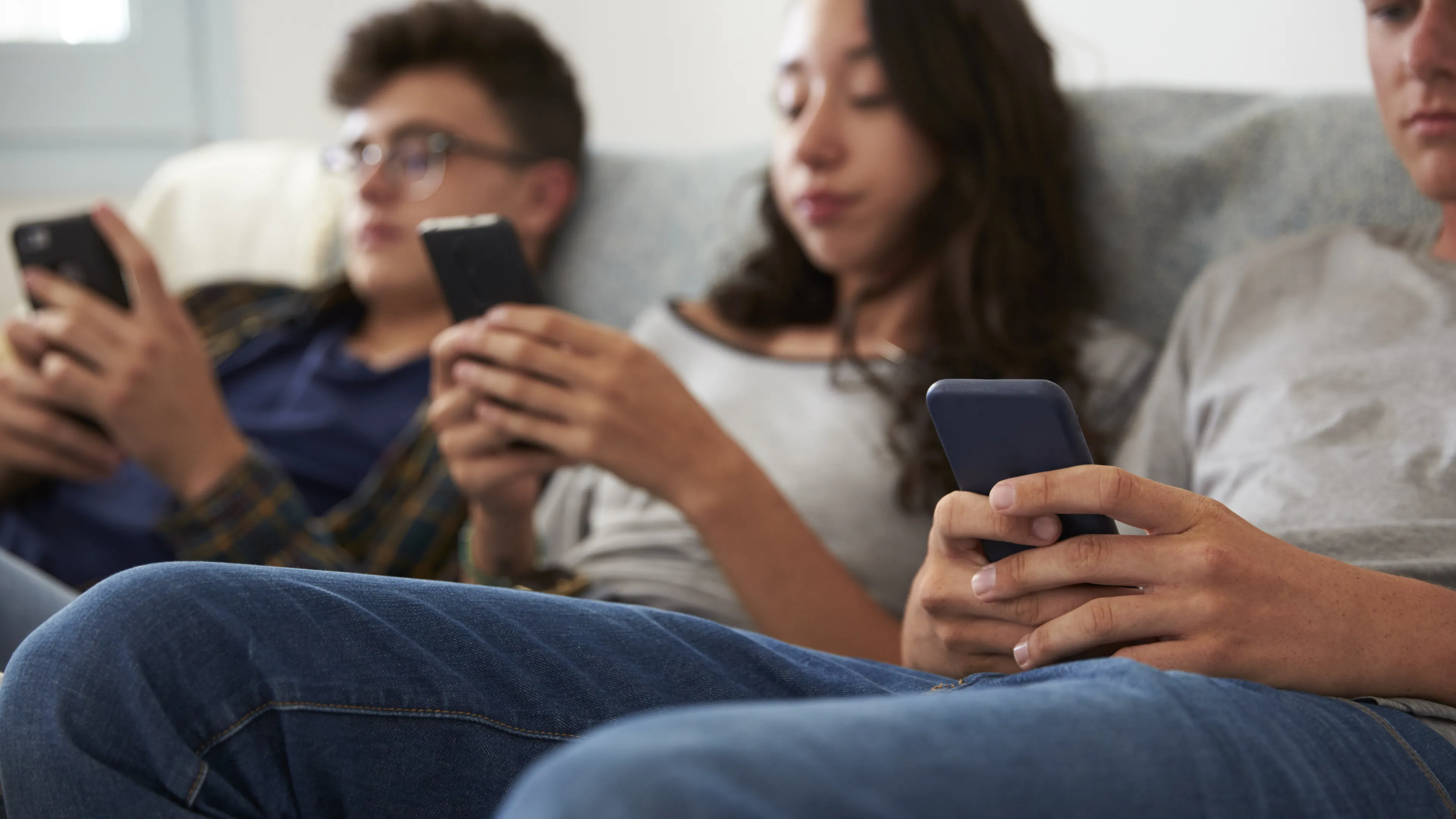 Three teenagers are sitting on the couch looking at their phones - the image is out of focus.
