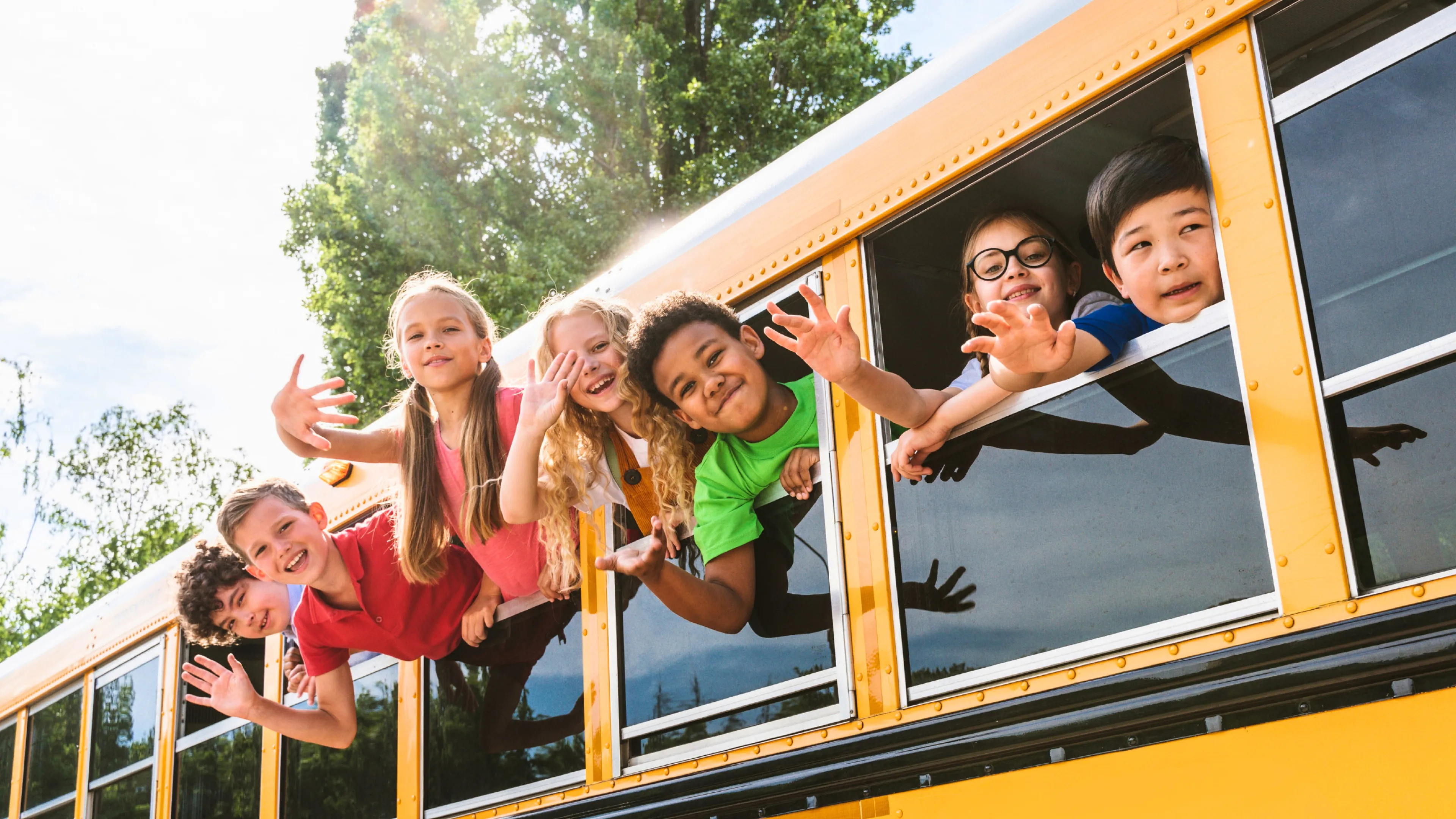Group of kids smiling and waving from school bus