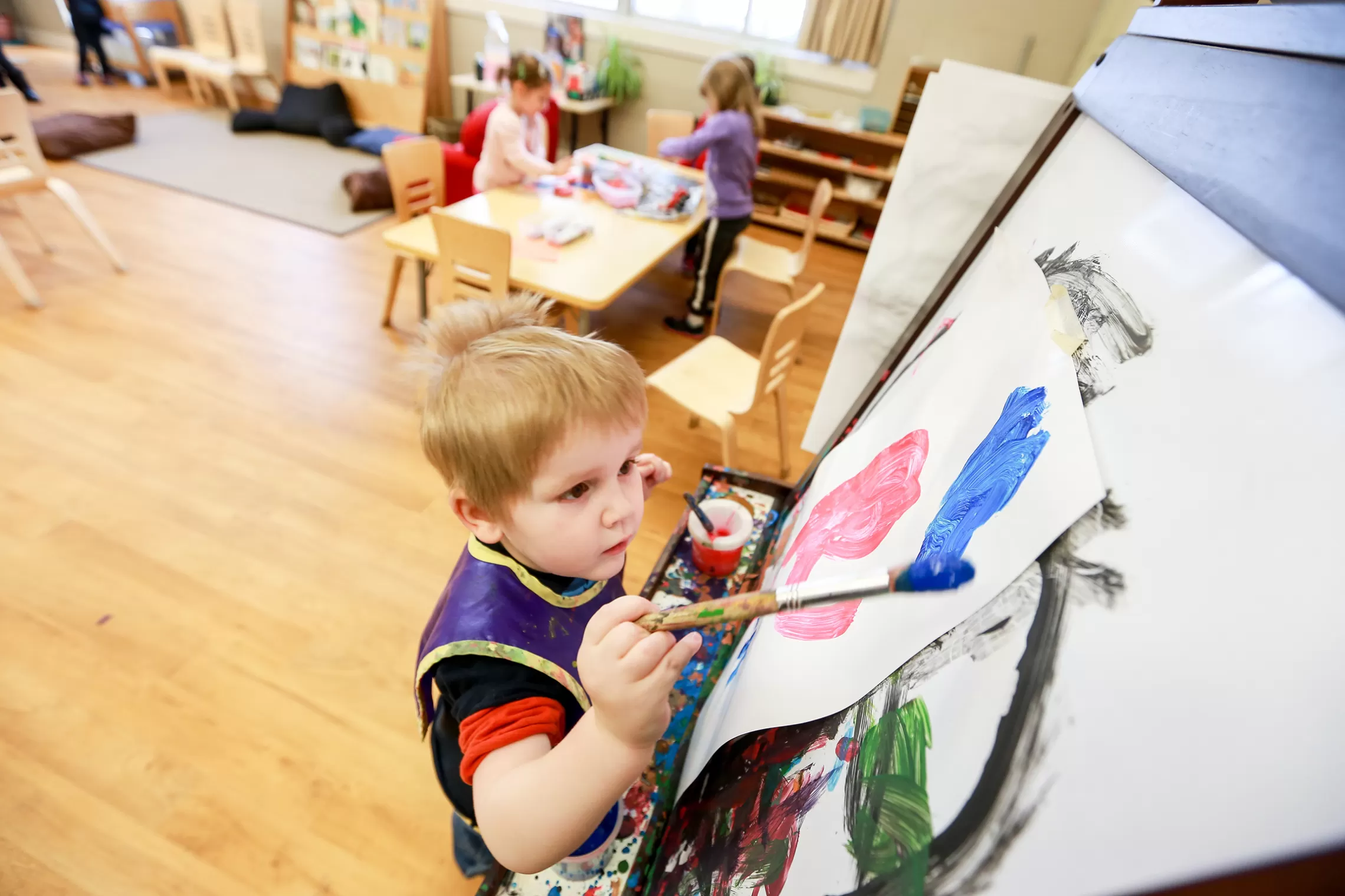 Male preschool child painting with a brush at an easel