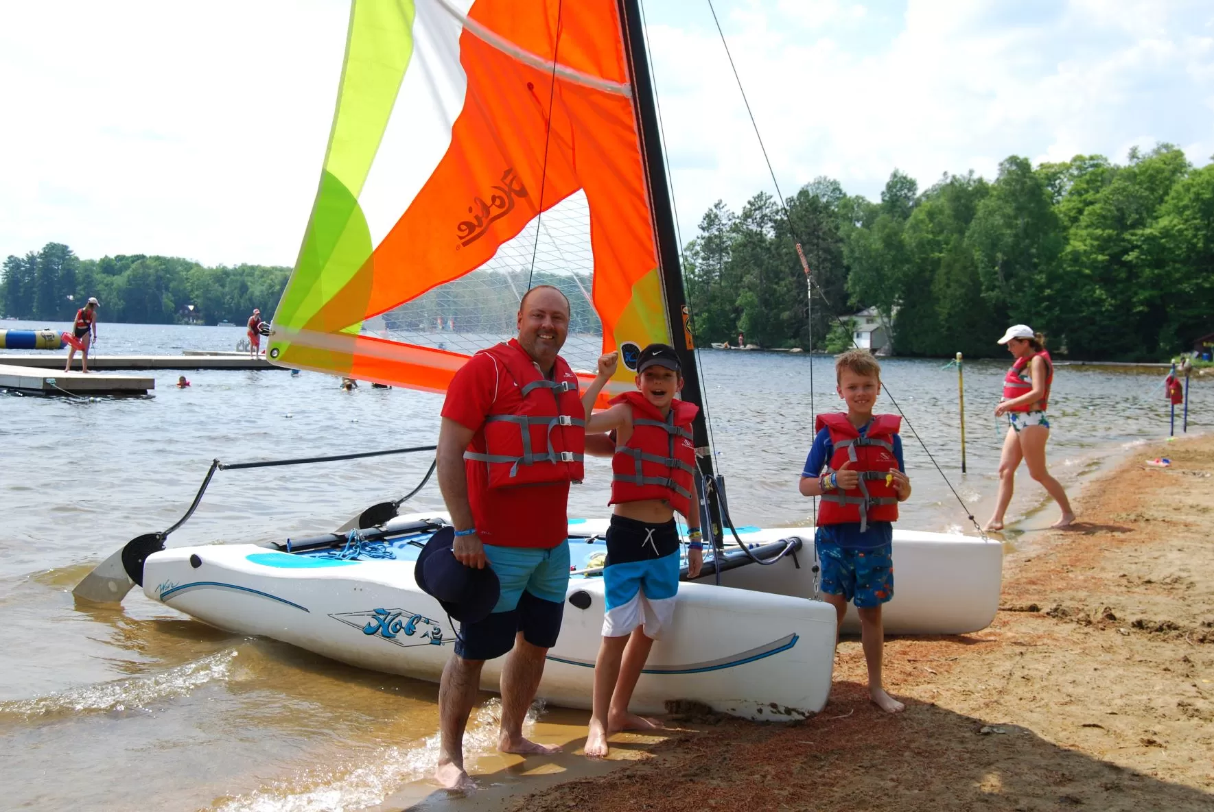 Father and sons standing in front of hobie cat on water