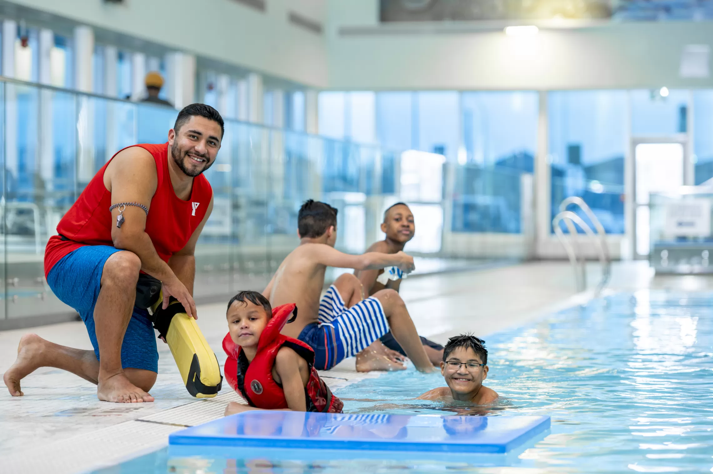 Lifeguard kneeling on deck beside children in the pool
